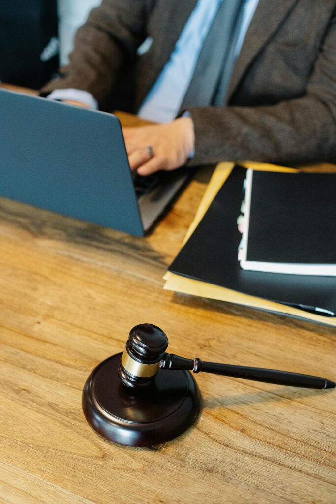 From above of crop anonymous male lawyer in formal clothes typing on laptop while sitting at wooden table with stack of documents and gavel